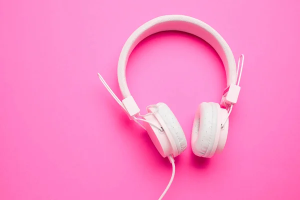 White headphones with cord on an empty pink background.