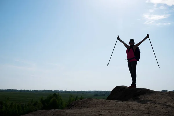 Foto de mulher turística com braços levantados com paus para caminhar contra o sol — Fotografia de Stock