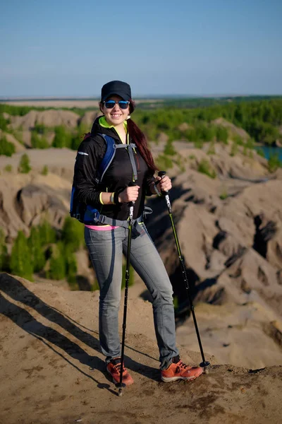 Foto van lachende toeristische meisje met rugzak en wandelen stokken op heuvel — Stockfoto