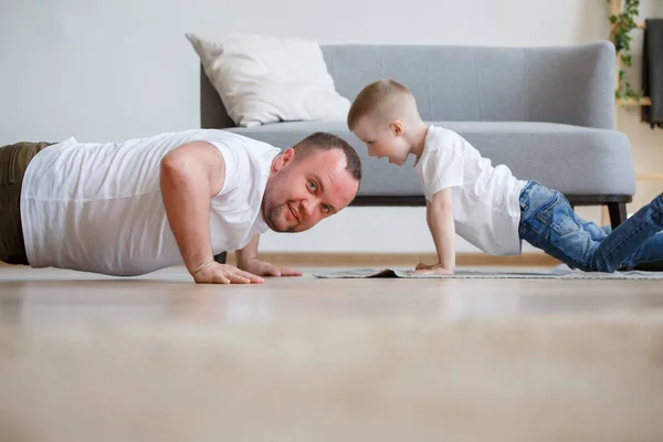 Fotolibro de padre e hijo empujando en el suelo cerca del sofá — Foto de Stock