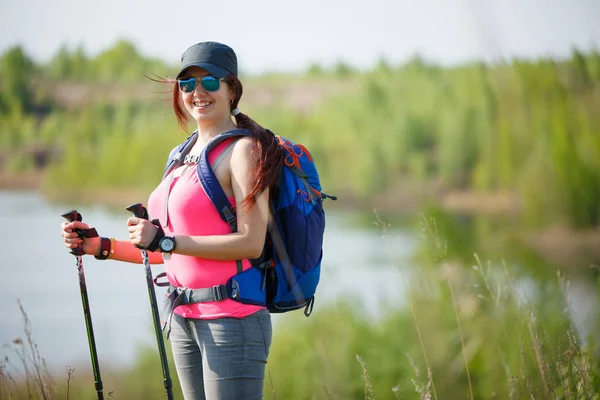 Image of sporty woman with walking sticks on background of lake and green vegetation — Stock Photo, Image