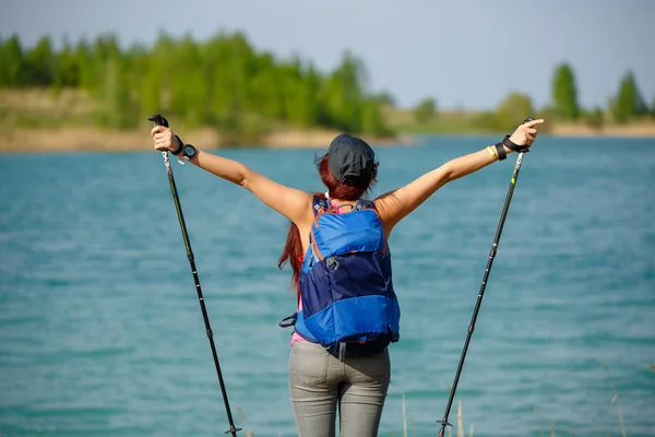 Immagine della schiena di donna sportiva con bastoni da passeggio e zaino sullo sfondo del lago — Foto Stock