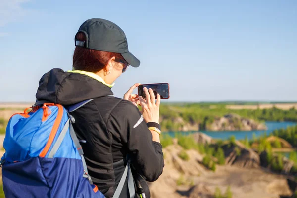 Foto von Touristenmädchen mit Rucksack fotografiert Smartphone, das auf Hügel steht — Stockfoto