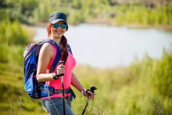 Foto di donna sportiva con bastoni da passeggio e zaino sullo sfondo di lago e vegetazione — Foto Stock