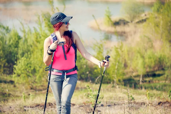 Immagine di giovane ragazza sportiva che distoglie lo sguardo con bastoni da passeggio sullo sfondo di lago e vegetazione verde — Foto Stock