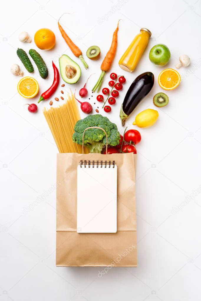 Photo of paper bag with vegetables, fruits and spaghetti . Empty notepad for text