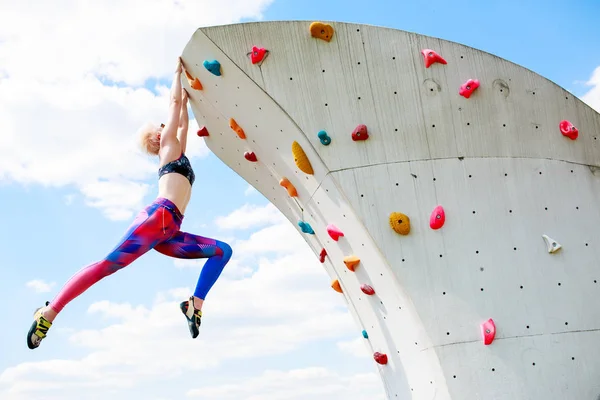 Foto von unten von Sportlerin in Leggings, die zum Klettern gegen blauen Himmel an der Wand hängt — Stockfoto