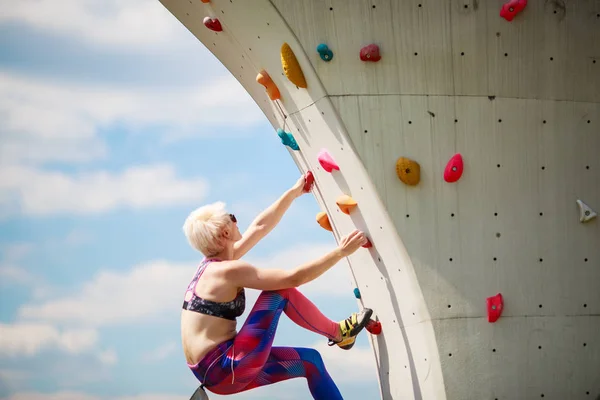 Fotografia sportowa kobiety w leginsach na ściany do wspinaczki przeciw błękitne niebo — Zdjęcie stockowe