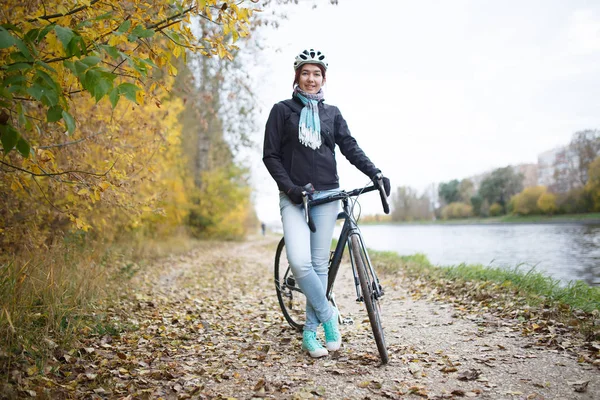 Girl in helmet riding bicycle on shore of river — Stock Photo, Image