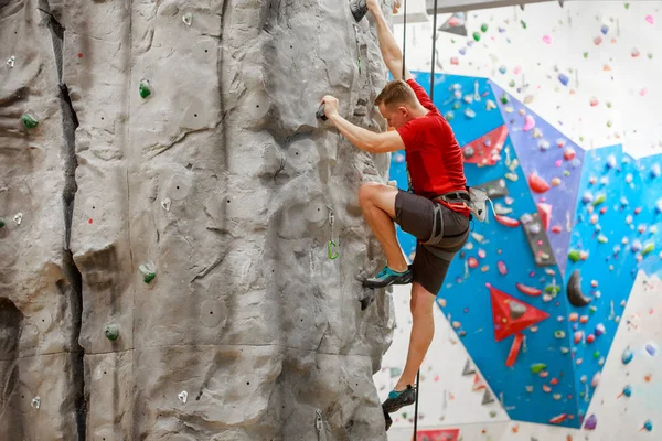 Foto von der Seite des Sportlers im roten T-Shirt beim Training an der Kletterwand drinnen — Stockfoto