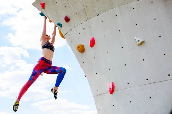 Zdjęcie od dołu dziewczyna sportowej w leginsach, wiszące na ścianie do wspinaczki przeciw błękitne niebo — Zdjęcie stockowe