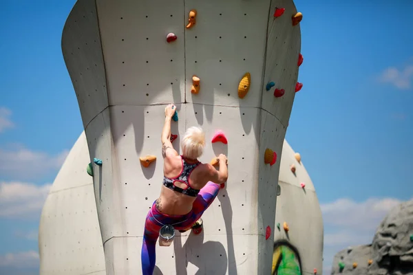 Photo from back of sports blonde in leggings on wall for rock climbing against blue sky — Stock Photo, Image