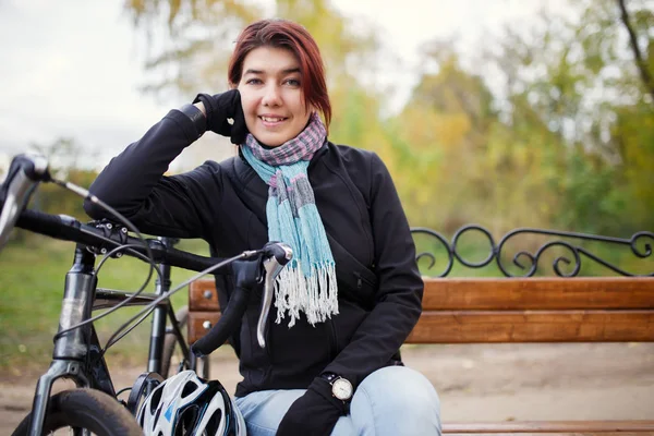 Foto di una ragazza sorridente seduta sulla panchina accanto alla bicicletta — Foto Stock