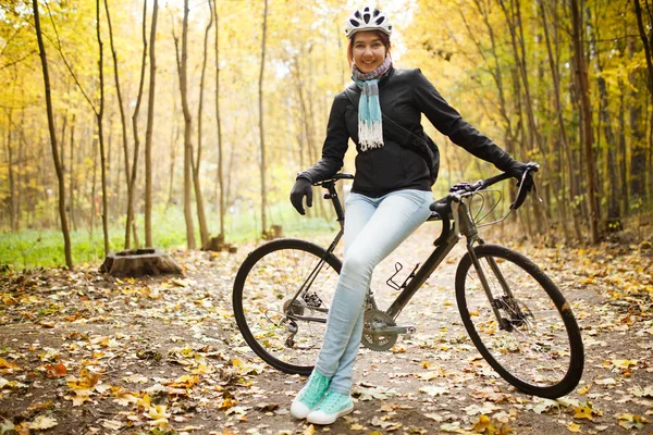 Foto da menina no capacete, jeans ao lado de bicicleta no parque de outono — Fotografia de Stock