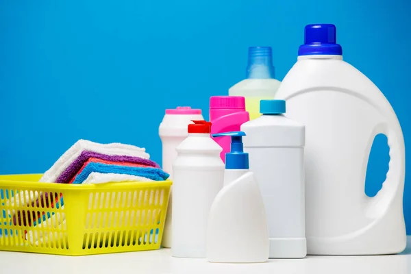Foto de varias botellas de productos de limpieza y toallas multicolores en cesta aislada sobre fondo azul — Foto de Stock