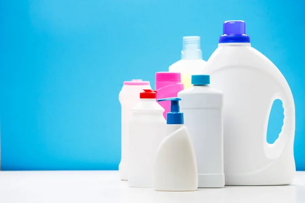 Foto di diverse bottiglie di prodotti per la pulizia su tavolo bianco isolato su sfondo blu, posto per iscrizione — Foto Stock