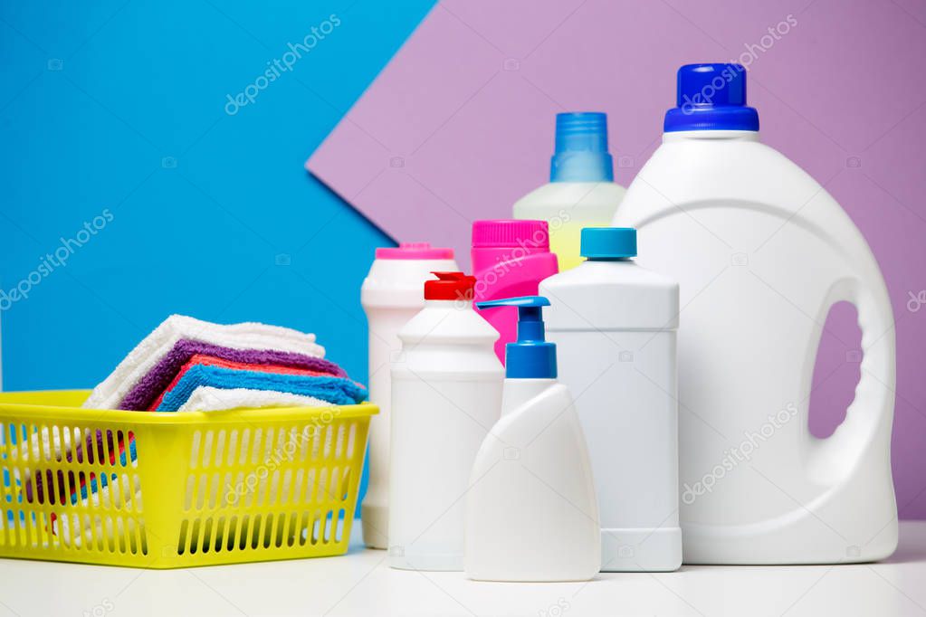 Photo of several bottles of cleaning products and multi-colored towels in basket isolated on violet,blue background