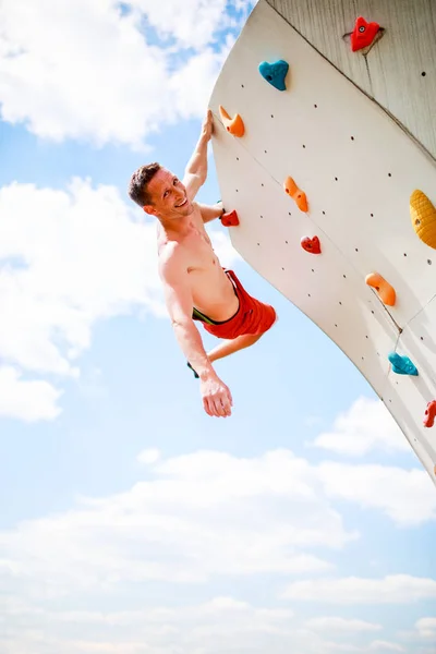 Foto do atleta sorrindo olhando para a câmera praticando na parede para escalada de rocha contra o céu azul com nuvens — Fotografia de Stock