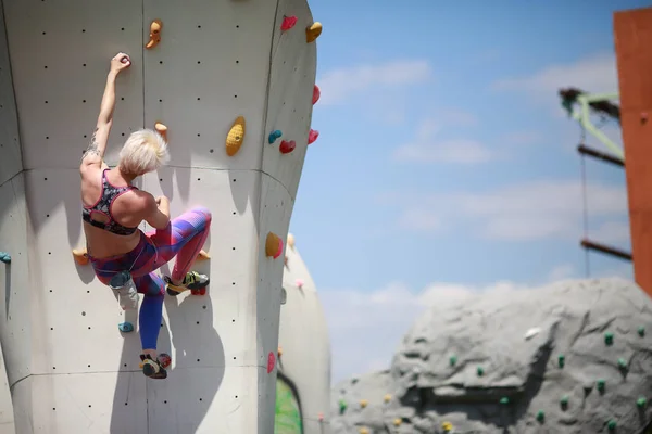 Foto von der Rückseite der jungen Blondine mit Kurzhaarschnitt in Sportkleidung üben an der Wand für Felsklettern gegen blauen Himmel — Stockfoto