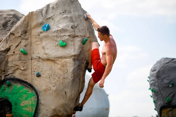 Foto von Sport-Brunet in roten Shorts, der auf Felsbrocken zum Klettern gegen bewölkten Himmel übt — Stockfoto