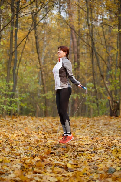 Full-length picture of athlete girl jumping with rope at autumn forest — Stock Photo, Image