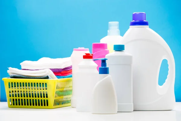 Foto de diferentes garrafas de produtos de limpeza e toalhas coloridas em cesta isolada no fundo azul — Fotografia de Stock