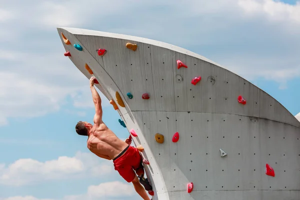 Foto vom Rücken eines jungen sportlichen Mannes in roten Shorts, der an der Wand hängt, um vor blauem Himmel mit Wolken zu klettern — Stockfoto