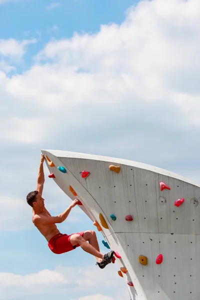 Foto von trainierten Sportlern in roten Shorts, die an einer Wand vor blauem Himmel mit Wolken Felsklettern üben — Stockfoto