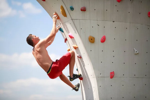 Foto eines Sportlers, der an einer Wand gegen bewölkten Himmel klettert — Stockfoto