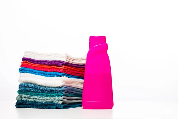 Foto de uma garrafa rosa de detergente e toalhas multicoloridas no fundo branco limpo — Fotografia de Stock