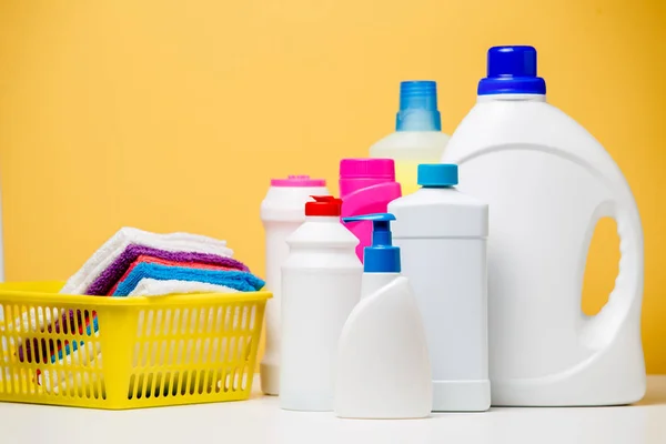 Foto de varias botellas de productos de limpieza y toallas multicolores en cesta aislada sobre fondo naranja — Foto de Stock