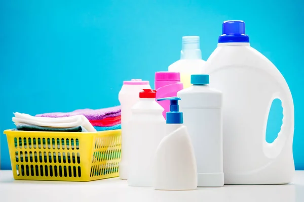 Foto de varias botellas de productos de limpieza y toallas de colores en cesta aislada sobre fondo azul — Foto de Stock