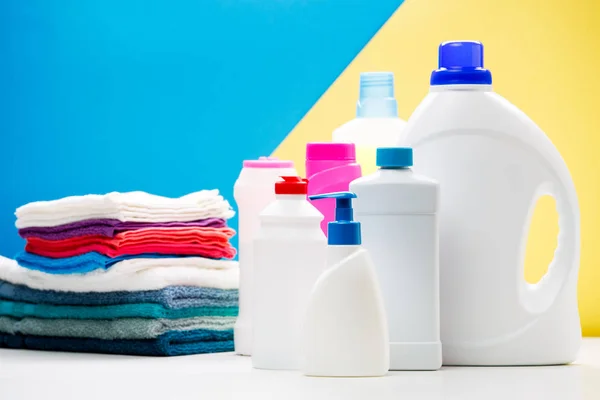 Foto av flera flaskor rengöringsprodukter och färgade handdukar på vitt bord isolerade på blå, gul bakgrund — Stockfoto