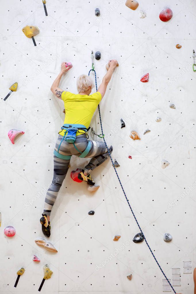 Photo from back of sports woman in yellow T-shirt scrambles up wall on workout