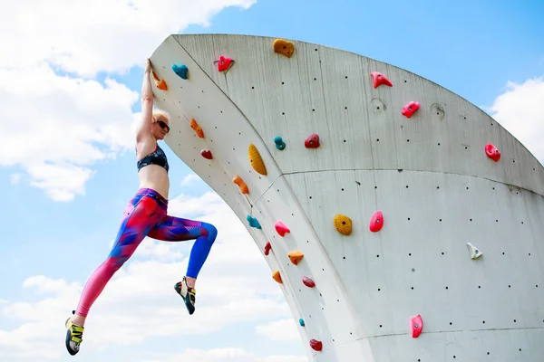 Foto einer sportlichen Frau in Leggings, die an der Wand hängt, um gegen den blauen Himmel zu klettern — Stockfoto