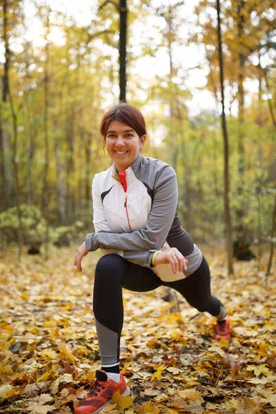 Podzimní fotografie sportovní ženy, táhnoucí se v lese na ranní pozadí stromů — Stock fotografie