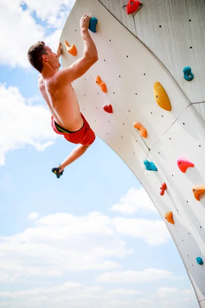 Foto de homem esportivo se exercitando na parede para subir contra o céu nublado — Fotografia de Stock
