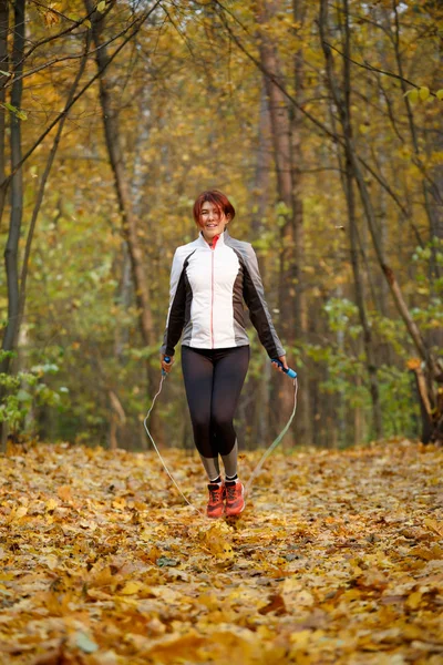 Foto van sport brunette springen met touw in herfst bos — Stockfoto