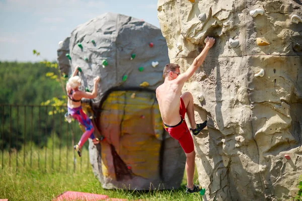 Foto eines Sportlers in roten Shorts und einer Frau beim Klettern auf Felsbrocken vor blauem Himmel mit Wolken — Stockfoto