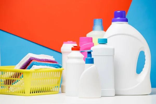 Foto de várias garrafas de produtos de limpeza e toalhas multicoloridas em cesta isolada em fundo vermelho e azul — Fotografia de Stock