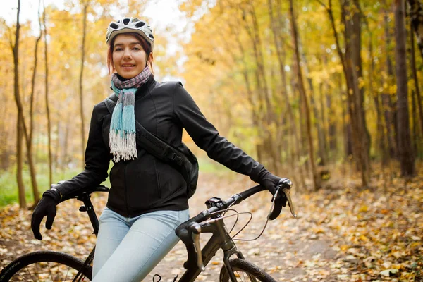 Portrait of brunette in helmet, jeans next to bicycle in autumn park — Stock Photo, Image