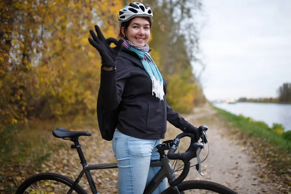 Foto di ragazza sorridente in casco e con zaino che mostra ok in bicicletta — Foto Stock