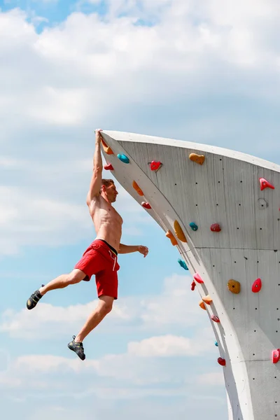 Foto eines jungen sportlichen Mannes, der im Sommer von einer Kletterwand hängt — Stockfoto