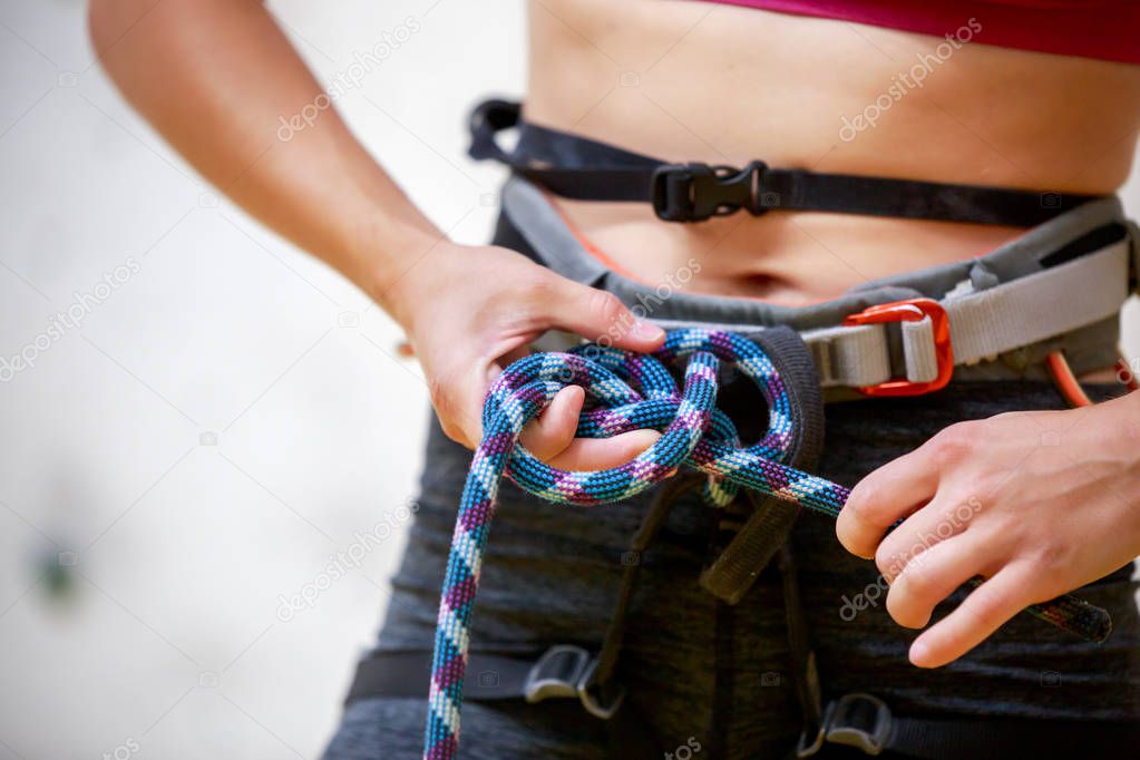 Close-up photo of athlete girl climber with safety rope in hands at gym