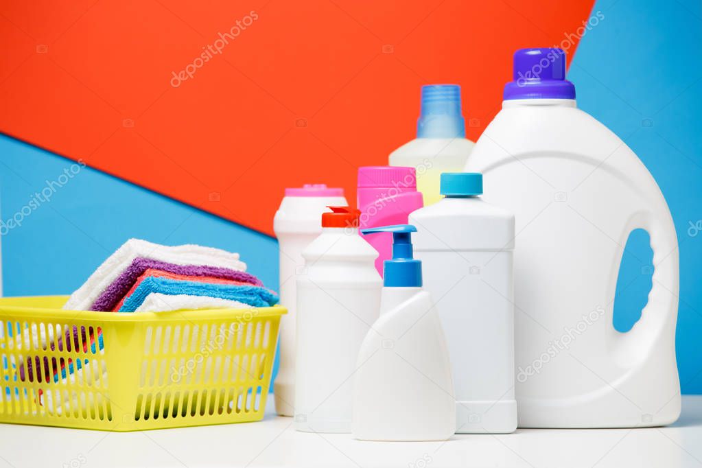 Photo of several bottles of cleaning products and multi-colored towels in basket isolated on red,blue background