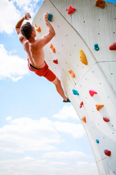 Foto da parte de trás do homem esportivo se exercitando na parede para subir contra o céu nublado — Fotografia de Stock