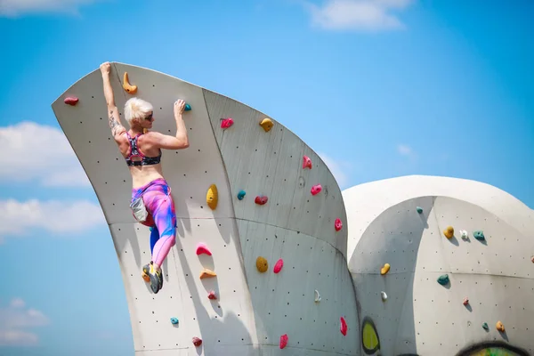 Foto von hinten von jungen athletischen Mädchen in Leggings, die an der Wand hängen, um gegen den blauen Himmel zu klettern — Stockfoto