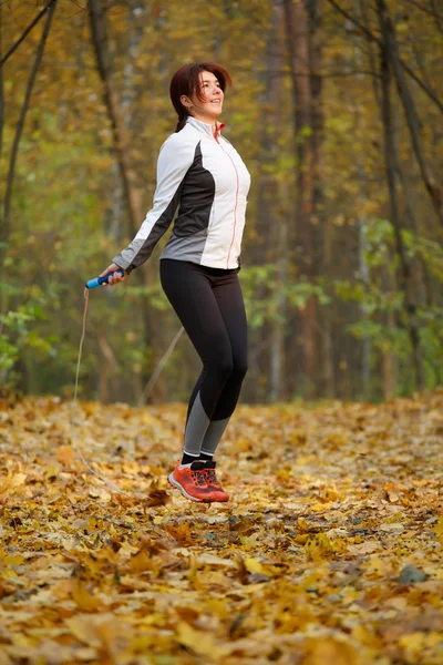 Photo of side view of sporty brunette jumping with rope at autumn forest — Stock Photo, Image