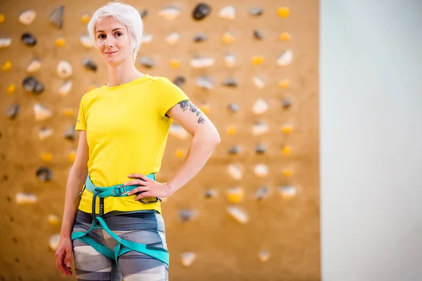 Photo of young woman in sports clothes and safety belts on climbing wall in sports hall — Stock Photo, Image