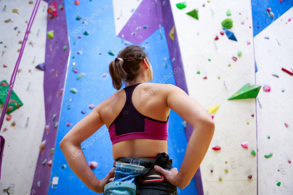 Photo of young athlete woman from back with hands on waist-standing next to wall for rock climbing